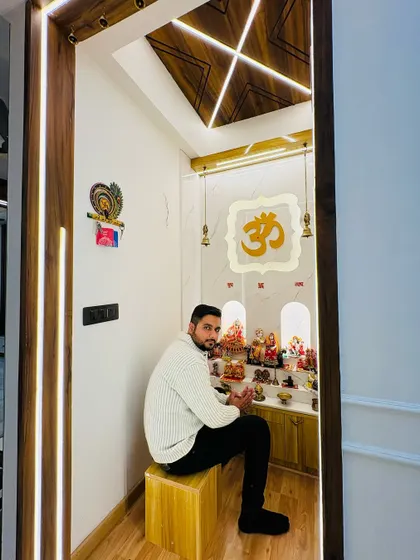 Sitting in a serene mandir we designed. This space features a backlit 'Om' symbol, a wooden-paneled ceiling, and ample space for idols and prayer essentials.