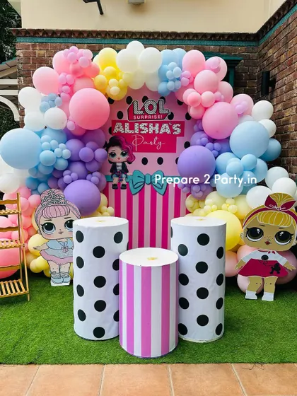 An LOL Surprise theme party with a vibrant pastel balloon arch and character cutouts. The backdrop features pink stripes and polka dots, perfectly matching the fun and fashionable dolls.