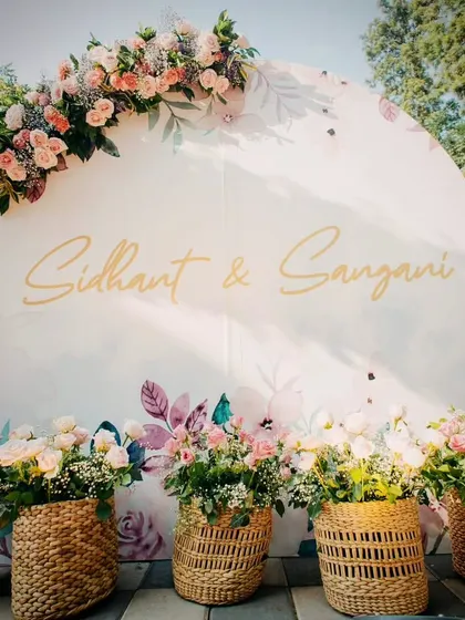A beautiful welcome sign for the Mehendi, featuring a pastel floral design and elegant calligraphy, set against a backdrop of woven baskets filled with flowers.