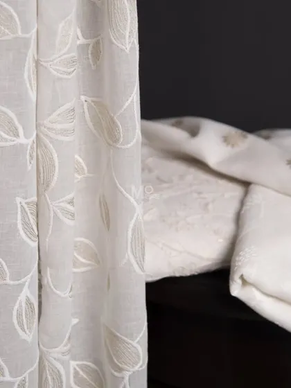 Our handpicked sheer fabric collection in neutral off-white and ivory tones. This image shows a curtain with embroidered leaves next to a stack of other sheer options.