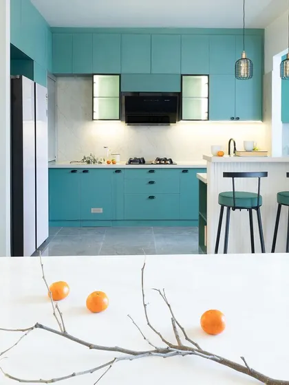 A wide view of the teal green kitchen, showing the open layout and cozy breakfast nook. The pendant drop lights over the counter bring a warm, inviting glow to the space.