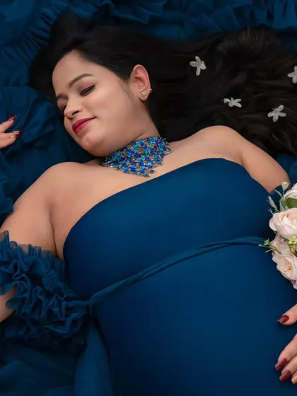 A dreamy, artistic portrait. Lying amidst a sea of deep blue fabric, this mother-to-be looks serene, with delicate flowers in her hair. This overhead shot creates a unique, painterly effect for a fine art pregnancy portrait.