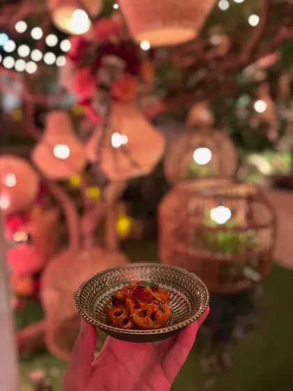 A small bowl of a flavourful appetizer, held amidst the warm, festive glow of an anniversary party's decor.