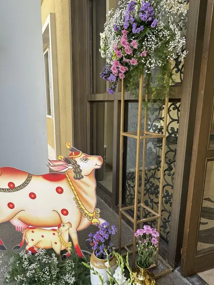 A traditional Pichwai cow and calf cutout stands at the entrance, paired with a modern floral stand, beautifully merging sacred art with contemporary styling.