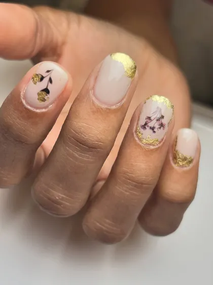 A close-up of the delicate dried flower and gold foil nail art. Each nail is a unique composition, making the set a true work of art.