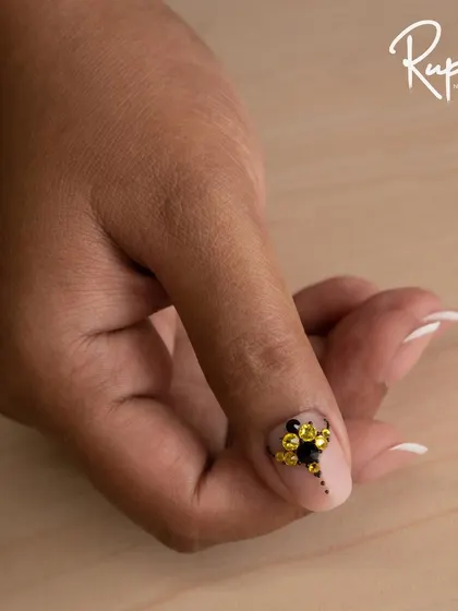 A close-up of a custom jewelry design on a client's thumb, featuring a cluster of black and yellow crystals.