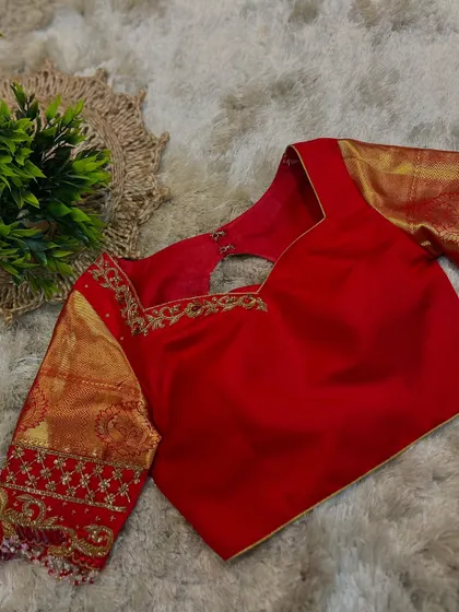 A classic red bridal blouse with gold zari work on the sleeves. The square neckline and back cutout add a modern touch.