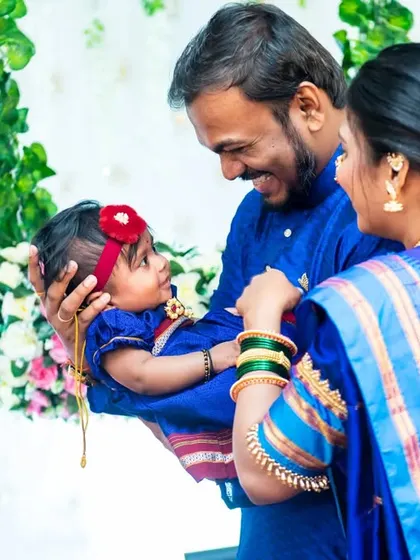 A beautiful moment from a naming ceremony. The parents look lovingly at their newborn, all dressed in matching royal blue traditional outfits. It's a perfect family portrait.