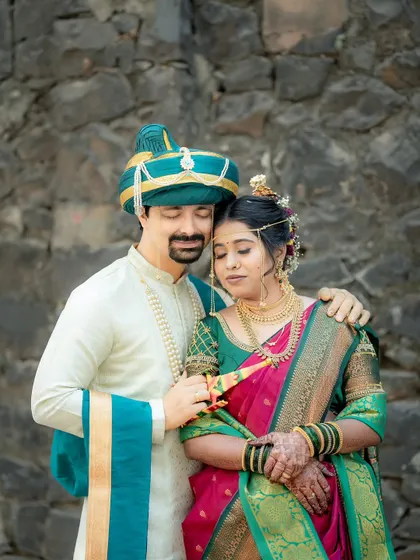 An intimate portrait of a Maharashtrian couple against a rustic stone wall, highlighting the rich colors of their traditional wedding clothes.