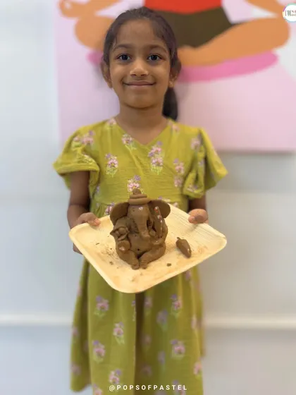 The proud smile of a young artist holding her finished clay Ganesha. Our workshops are designed to build confidence and let little hands create big, beautiful things.