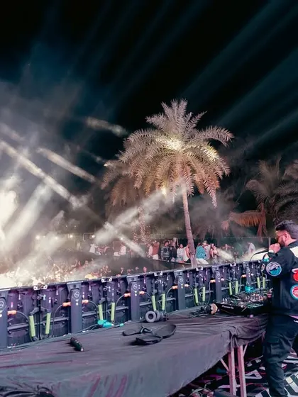 A wide shot of the stage at a Daman beach festival, with palm trees and massive light rigs creating a unique vibe.
