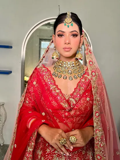 The front-facing portrait shows the symmetry and precision of the makeup application. The emerald green in the maang tikka adds a beautiful contrast to the red, a detail we can highlight with subtle color choices in the makeup.