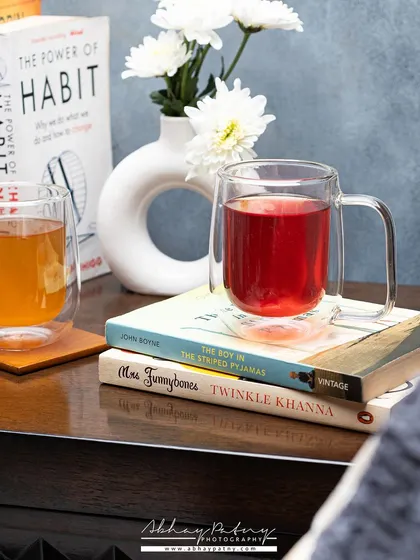 A cozy, lifestyle shot of two cups of tea in a comfortable setting. Placing the mugs on books suggests a relaxing moment, creating an emotional connection with the viewer.