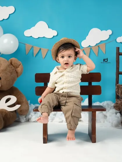 This little one is ready for his teddy bear picnic-themed first birthday. The blue sky backdrop and fluffy clouds create a cheerful setting.