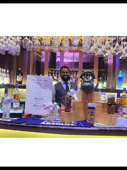 A fully stocked bar ready for service. This wide shot shows the extensive selection of spirits, glassware hanging from above, and our bartender ready to welcome guests.