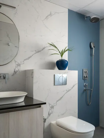 The bathroom design combines classic marble-look tiles with a bold blue accent wall in the shower area. This creates a fresh, modern look that is both luxurious and easy to maintain.
