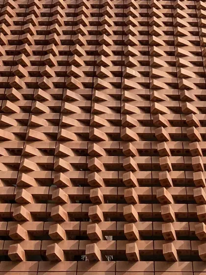 A close-up of the parametric brick facade of the 'Brick Weave House'. The bricks are rotated at varying angles to create a dynamic, textured surface that plays with light and shadow.
