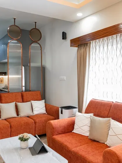 A vibrant living room with burnt-orange sofas and a unique three-panel mirror partition. This setup shows how a decorative divider can separate spaces while maintaining an open and airy feel.