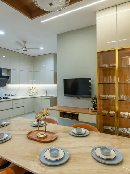 The dining area is equipped with a custom crockery unit that has glass-front shutters and gold accents. This unit provides elegant storage and display space, complementing the modern dining set.