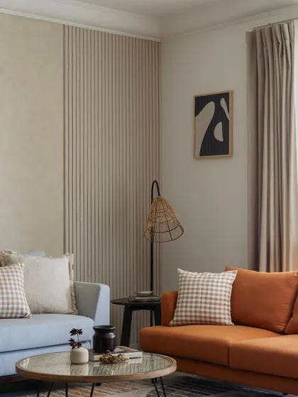 This living room celebrates minimalism with earthy tones and subtle textures. The combination of a powder blue and a burnt orange sofa adds warmth, while the fluted and lime-washed wall panels provide a tactile backdrop.