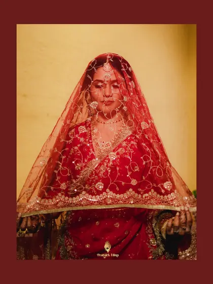 The bride holds her sheer red veil, her expression serene and thoughtful. This portrait captures the traditional beauty and quiet grace of the moment.
