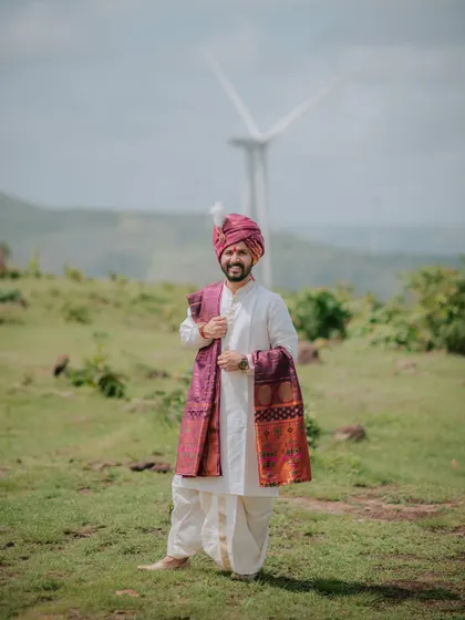 A portrait of the groom in traditional Maharashtrian attire against a scenic backdrop with windmills.