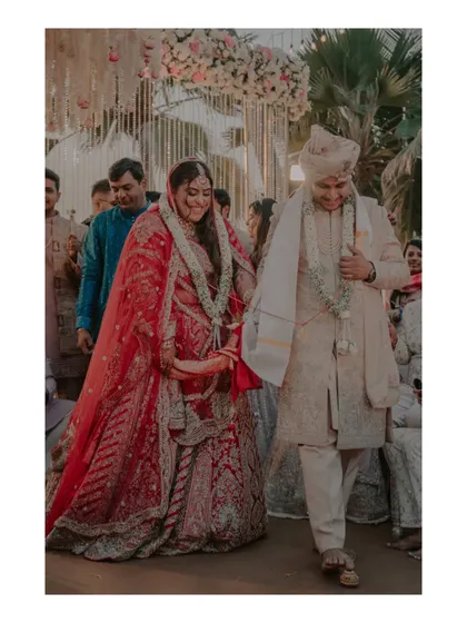 The couple walks hand-in-hand after their wedding ceremony, smiling, surrounded by their happy families.