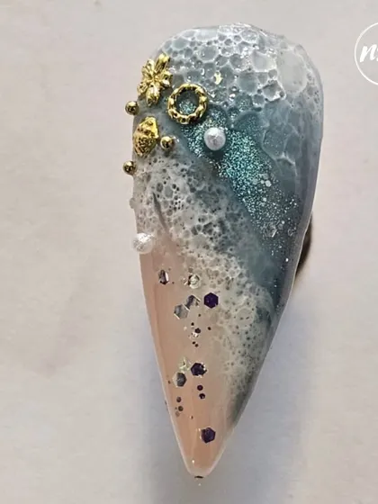 This textured ocean-themed nail is a piece of art. A student created this look, combining glitter, sand effects, and sculpted details to evoke a beach scene.