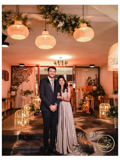 The couple posing in a beautifully designed space with boho-chic decor, including rattan lamps and birdcage lanterns.