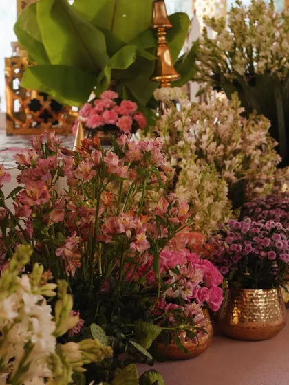A close-up of the vibrant floral arrangements at the base of the mandap, featuring a mix of pinks, whites, and purples in elegant brass pots.