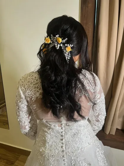 A view of the elegant hairstyle created for a Christian bride. Soft curls are gathered at the back and adorned with delicate yellow flowers and pearls, perfectly matching her white lace gown.