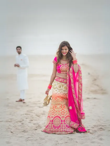 A candid and artistic shot of the bride on the beach, with the groom softly focused in the background. It tells a story of love and connection in a subtle, beautiful way.