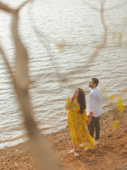 A beautiful shot of the couple by the water, framed by tree branches, creating a natural and artistic composition.
