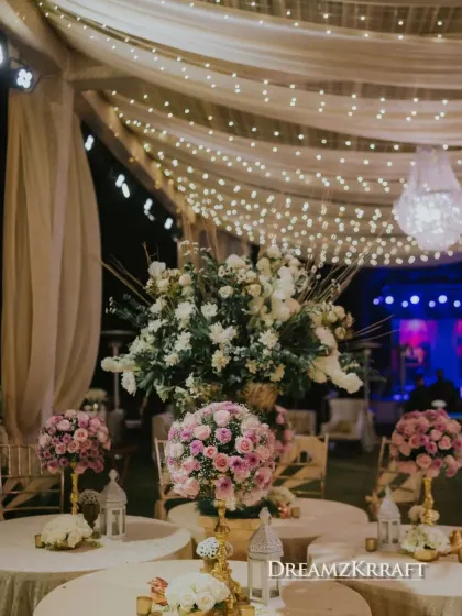 A beautiful seating arrangement for a Sufi night, with tables adorned with pink and white rose centerpieces under a canopy of fairy lights. The design feels both grand and intimate.
