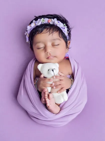 A newborn cuddling a tiny white teddy bear. Using simple props like this adds a touch of sweetness and innocence to the portrait.