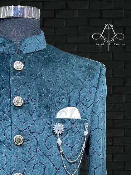 A detailed shot of a teal velvet bandhgala with a modern geometric pattern. The custom buttons and elegant lapel chain brooch add a layer of personality, making it perfect for a stylish groom or wedding guest.