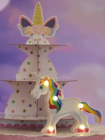 A close-up of unicorn-themed party props, including a multi-tiered cupcake stand and a light-up unicorn figurine.