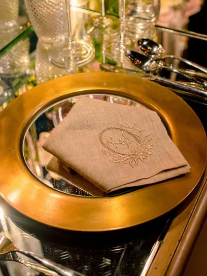 A close-up of a gold charger plate with a mirrored surface and a custom embroidered napkin.
