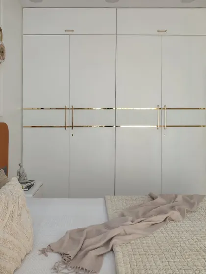 A close-up of the sleek white wardrobe with minimalist gold inlay and handles. This design provides ample storage while maintaining a clean, sophisticated aesthetic.