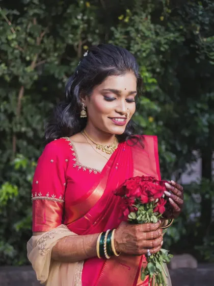 The bride holds a bouquet of red roses, her gentle smile and beautiful saree creating a classic and romantic portrait.