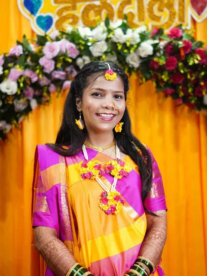 A smiling portrait of the bride at her Haldi ceremony, set against a vibrant yellow and floral backdrop.