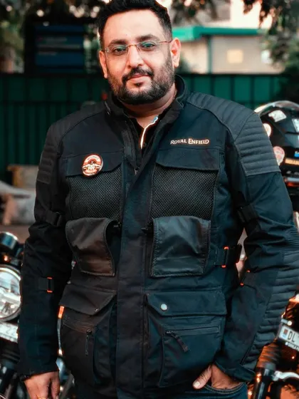 A portrait of a Royal Enfield community influencer at a tribe meetup. The image captures his friendly demeanor and official riding jacket, representing the leadership within the biker group.