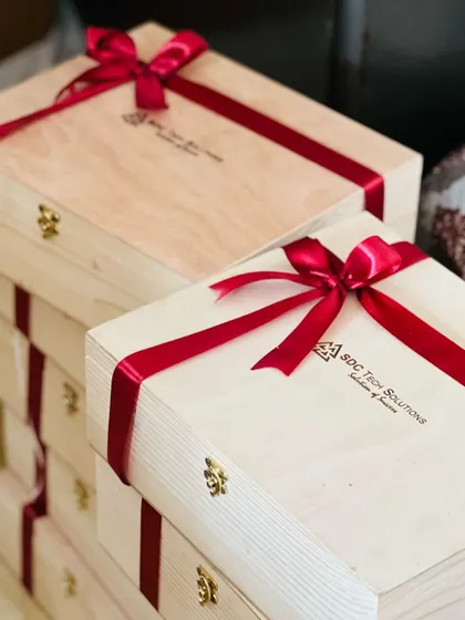 A stack of corporate Diwali gifts for 'SDC Tech Solutions'. The wooden boxes are branded with the company logo and tied with a festive red ribbon, ready to be gifted to employees or clients.