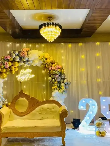 Celebrating a silver jubilee with style. This 25th-anniversary setup includes a beautiful balloon arch in gold and silver, a "Better Together" neon sign, large marquee numbers, and elegant seating.