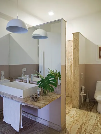 The bathroom continues the minimalist theme with clean lines and natural materials. A marble countertop and flooring add texture and an earthy element, while the simple white vessel sink and pendant lights maintain a modern, uncluttered feel.