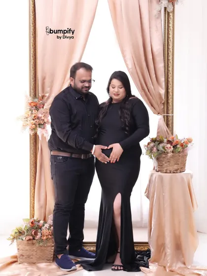 A classic studio maternity portrait. The couple forms a heart with their hands on the baby bump, a sweet symbol of their growing love.