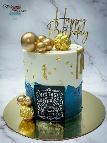 A 40th birthday milestone cake with a vintage "Aged to Perfection" theme. This buttercream cake combines a deep blue with white and gold for a masculine and stylish look.