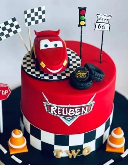 A custom cake inspired by the movie 'Cars' for Reuben's second birthday. Complete with Lightning McQueen, traffic signs, and checkered flags, it's a dream cake for any young fan.