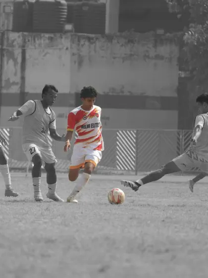 A player in our red and white kit skillfully maneuvering the ball under pressure from multiple opponents during a competitive match.
