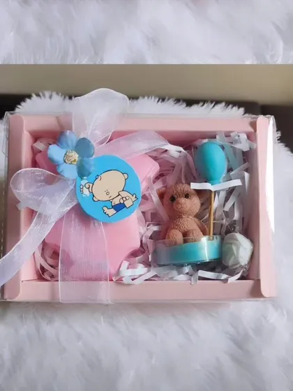 A cute baby shower return favor box, containing a baby romper soap and a teddy bear candle.